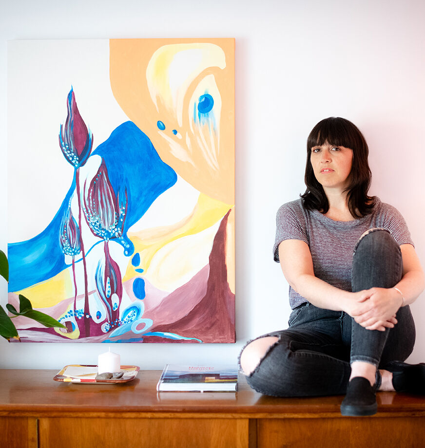 Florence Hupin assise devant une grande œuvre d'art colorée dans un espace de travail
